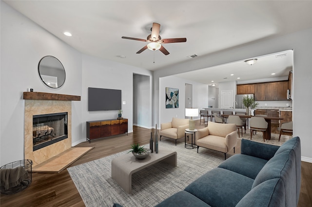 living room featuring ceiling fan, light wood-type flooring, and a tile fireplace