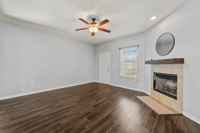 unfurnished living room with ceiling fan, a tiled fireplace, and dark hardwood / wood-style floors