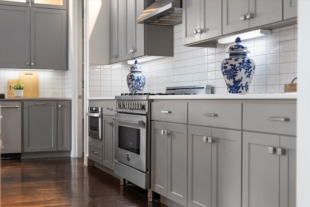 kitchen with decorative backsplash, wall chimney exhaust hood, dark wood-type flooring, and stainless steel appliances