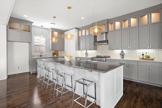 kitchen featuring a center island, decorative light fixtures, range, wall chimney exhaust hood, and a breakfast bar area