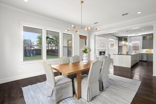 dining space with an inviting chandelier, ornamental molding, plenty of natural light, and dark wood-type flooring