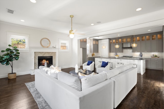 living room featuring ceiling fan, a tile fireplace, crown molding, and dark hardwood / wood-style flooring