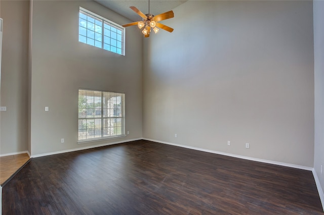 spare room featuring a towering ceiling, ceiling fan, and dark wood-type flooring