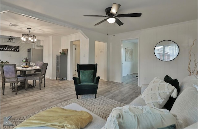 living room with ceiling fan with notable chandelier, light hardwood / wood-style flooring, and crown molding