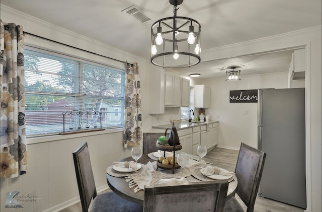 dining area with a notable chandelier, crown molding, light hardwood / wood-style floors, and sink