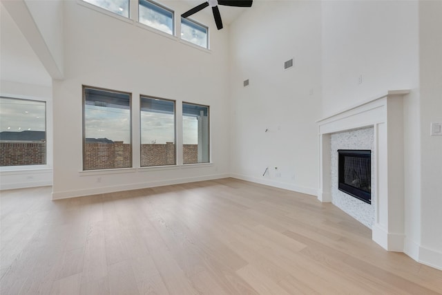 unfurnished living room featuring a tile fireplace, a towering ceiling, light hardwood / wood-style floors, and ceiling fan