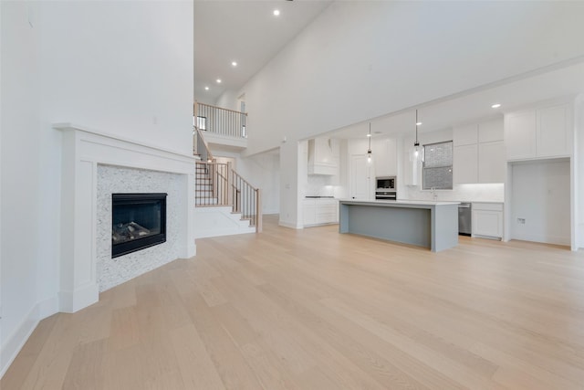 unfurnished living room featuring light wood-type flooring, sink, a towering ceiling, and a tiled fireplace