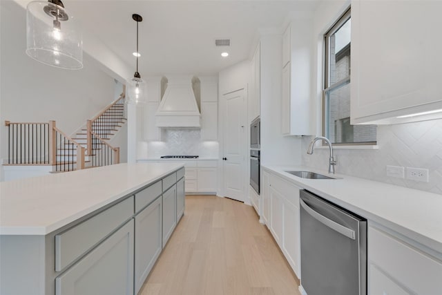 kitchen featuring premium range hood, hanging light fixtures, sink, light wood-type flooring, and stainless steel appliances