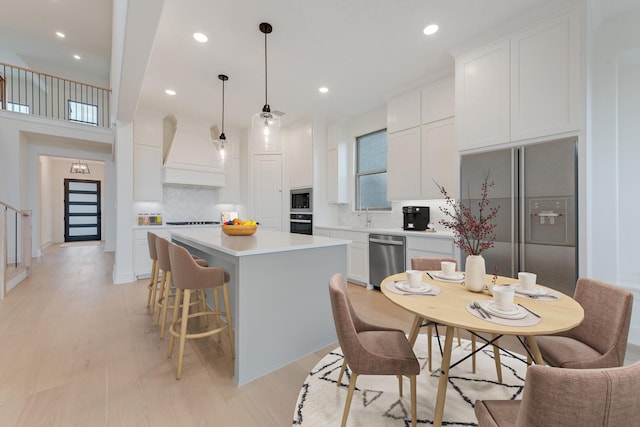 kitchen featuring white cabinetry, hanging light fixtures, stainless steel appliances, a kitchen island, and custom range hood