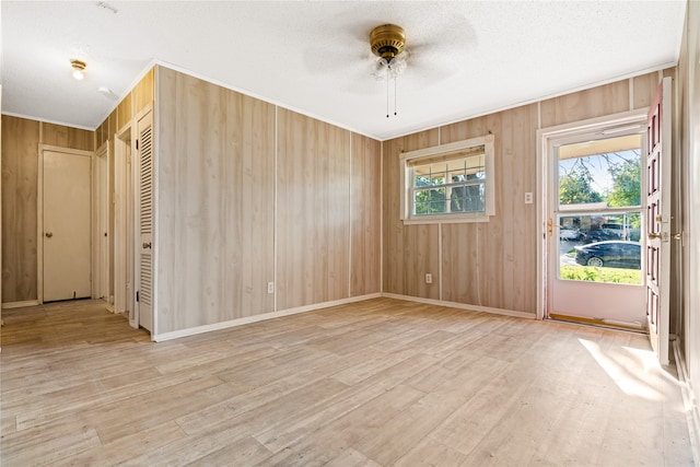 empty room featuring ceiling fan, wooden walls, light hardwood / wood-style flooring, and a wealth of natural light