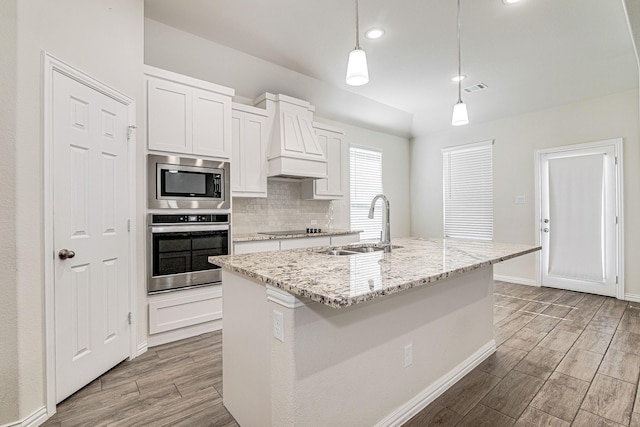 kitchen featuring a kitchen island with sink, sink, decorative light fixtures, and appliances with stainless steel finishes