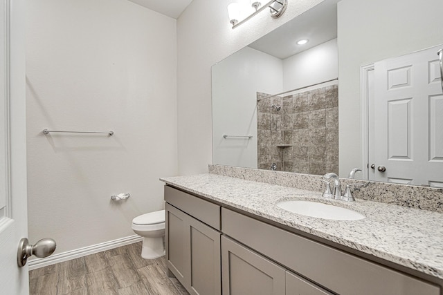 bathroom featuring hardwood / wood-style flooring, vanity, toilet, and tiled shower