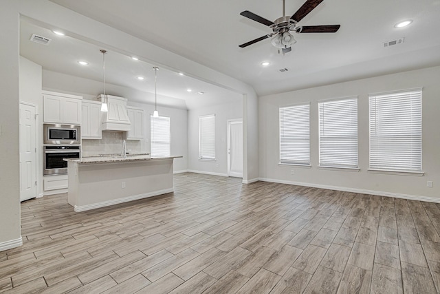 kitchen with hanging light fixtures, stainless steel appliances, light stone counters, a kitchen island with sink, and white cabinets