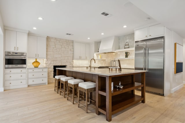 kitchen with custom exhaust hood, appliances with stainless steel finishes, light hardwood / wood-style floors, and white cabinetry