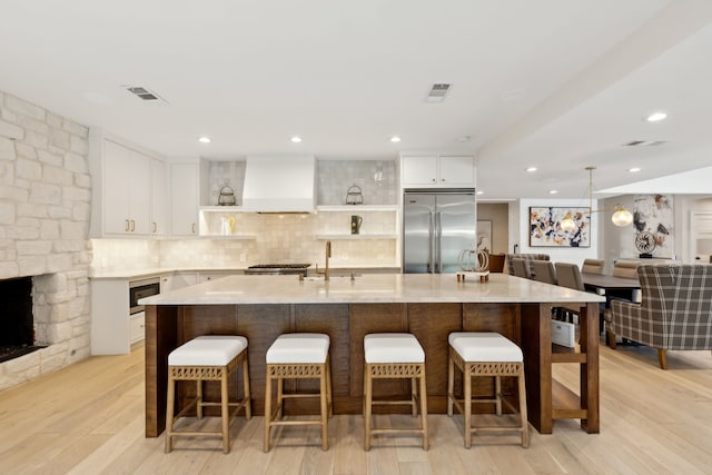 kitchen with light hardwood / wood-style flooring, white cabinetry, custom range hood, and built in appliances