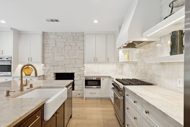 kitchen featuring white cabinets, custom exhaust hood, appliances with stainless steel finishes, and sink