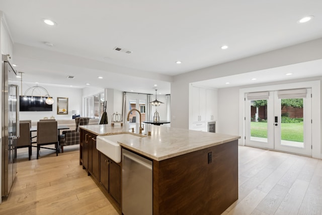 kitchen with an island with sink, sink, stainless steel dishwasher, light hardwood / wood-style floors, and light stone countertops