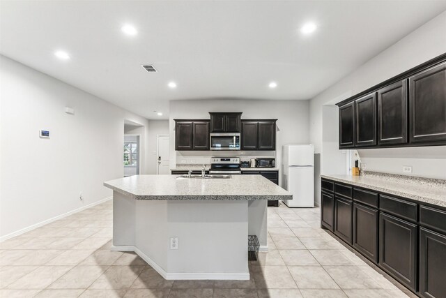 kitchen featuring sink, stainless steel appliances, a center island with sink, light tile patterned floors, and light stone countertops