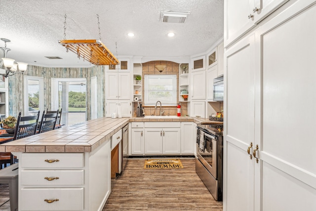 kitchen with hanging light fixtures, white cabinets, a textured ceiling, tile counters, and stainless steel electric range oven