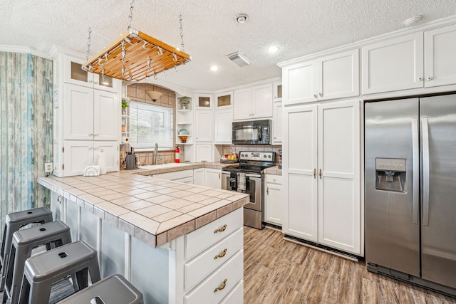 kitchen featuring stainless steel appliances, white cabinetry, tile counters, and hanging light fixtures