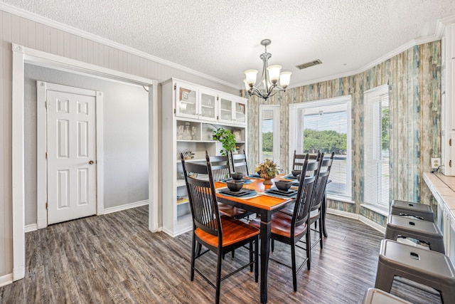 dining space with an inviting chandelier, a textured ceiling, dark wood-type flooring, and crown molding