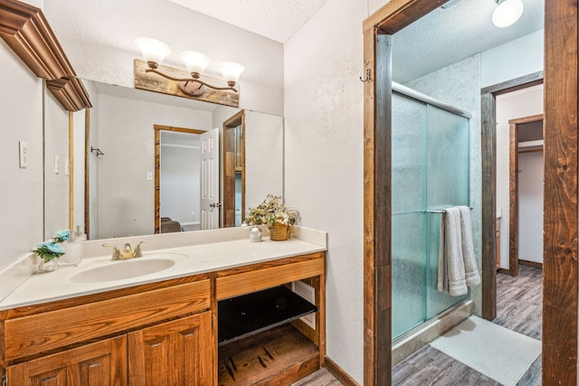 bathroom featuring a textured ceiling, wood-type flooring, vanity, and a shower with door