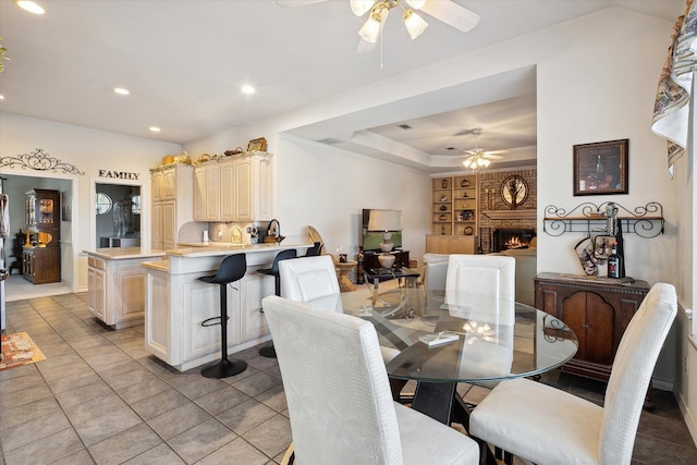 tiled dining area with a brick fireplace, a tray ceiling, built in shelves, and ceiling fan