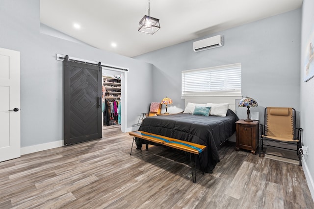 bedroom with wood-type flooring, a closet, a spacious closet, a barn door, and a wall unit AC