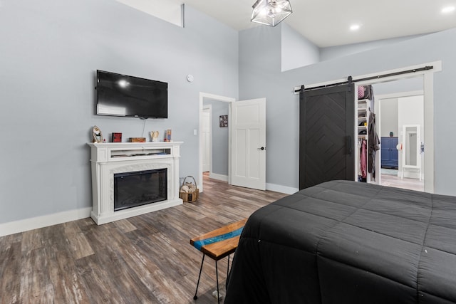 bedroom with hardwood / wood-style floors, a fireplace, a towering ceiling, and a barn door