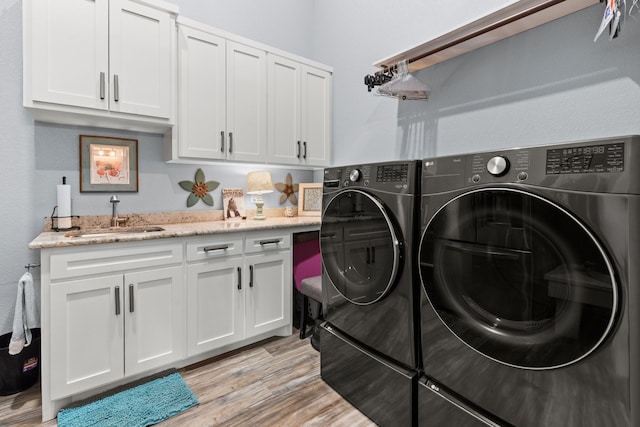 clothes washing area with light wood-type flooring, separate washer and dryer, sink, and cabinets