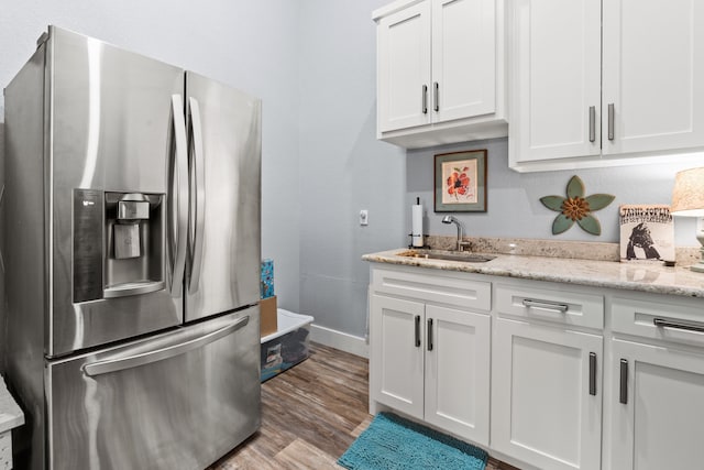 kitchen featuring light hardwood / wood-style floors, sink, white cabinets, light stone countertops, and stainless steel fridge