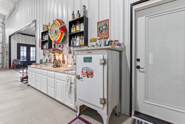 kitchen with light stone countertops, white cabinetry, french doors, and sink