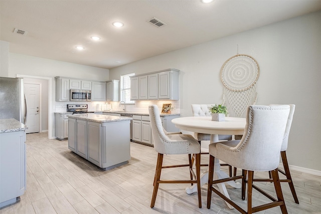 kitchen with gray cabinets, stainless steel appliances, backsplash, and a kitchen island