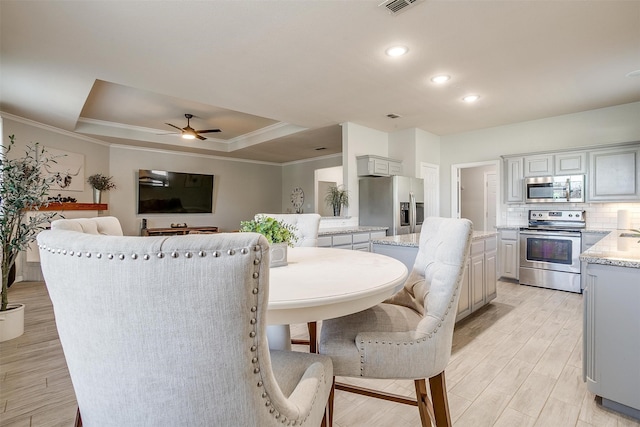 dining area featuring light wood-type flooring, a raised ceiling, crown molding, and ceiling fan