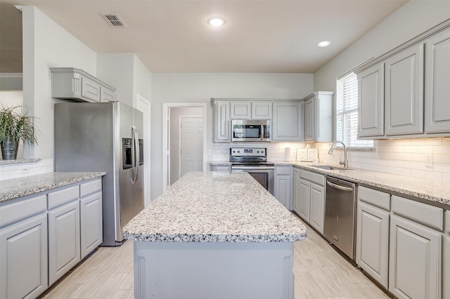 kitchen with light stone countertops, gray cabinets, stainless steel appliances, and a kitchen island