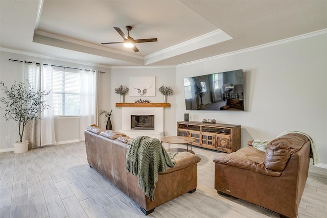 living room with a glass covered fireplace, a ceiling fan, a tray ceiling, and wood finished floors