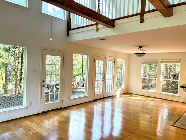 unfurnished living room with visible vents, plenty of natural light, a high ceiling, and hardwood / wood-style floors