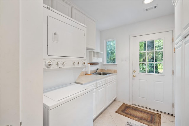 clothes washing area with a sink, stacked washer / dryer, light tile patterned floors, cabinet space, and visible vents