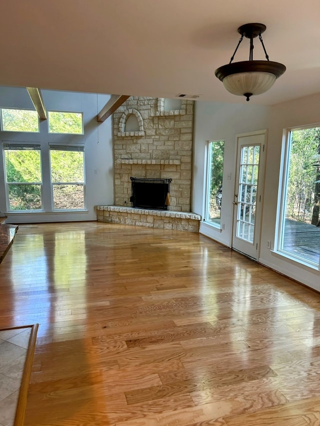 unfurnished living room featuring wood-type flooring, beamed ceiling, a fireplace, and plenty of natural light