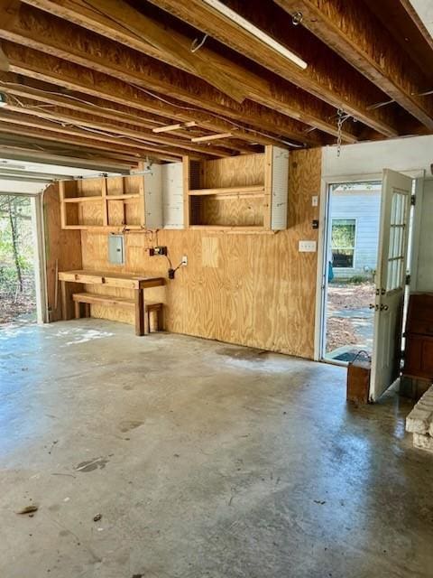 miscellaneous room featuring wooden walls, a wealth of natural light, electric panel, and unfinished concrete flooring