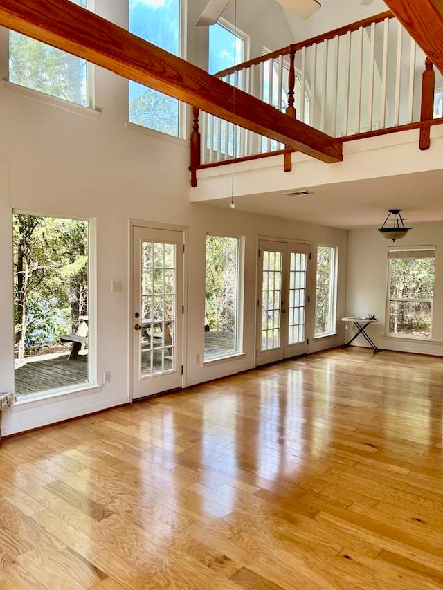 unfurnished living room featuring a towering ceiling, french doors, and light hardwood / wood-style flooring