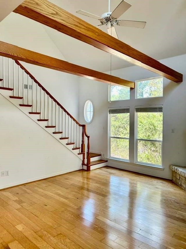unfurnished living room featuring stairway, hardwood / wood-style floors, a ceiling fan, and lofted ceiling with beams