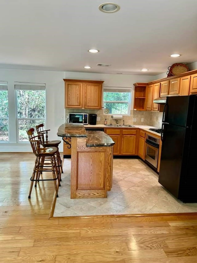 kitchen with light wood-type flooring, decorative backsplash, a center island, dark stone counters, and appliances with stainless steel finishes