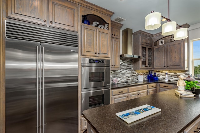 kitchen featuring appliances with stainless steel finishes, hanging light fixtures, tasteful backsplash, and wall chimney range hood