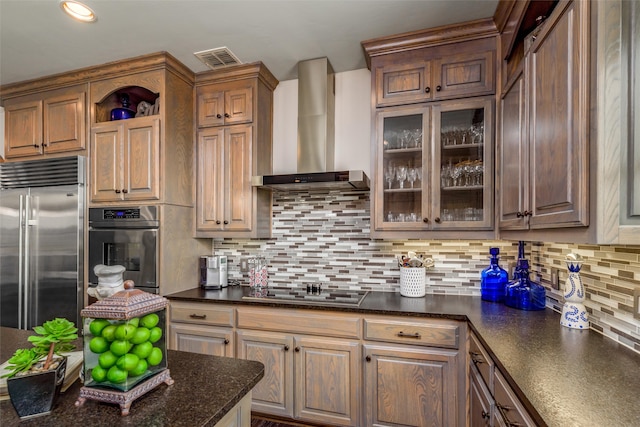 kitchen featuring dark stone countertops, appliances with stainless steel finishes, wall chimney range hood, and tasteful backsplash