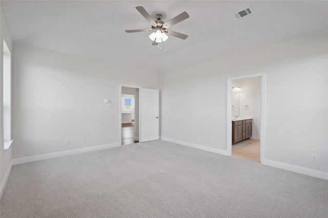 unfurnished bedroom featuring ceiling fan, light colored carpet, and ensuite bath