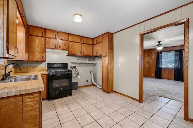 kitchen with wood walls, sink, black range with gas stovetop, ceiling fan, and light carpet