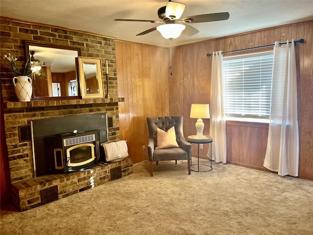 sitting room featuring ceiling fan, carpet flooring, a wood stove, and wooden walls