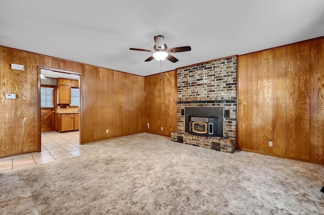 unfurnished living room featuring ceiling fan, light colored carpet, a wood stove, and wooden walls