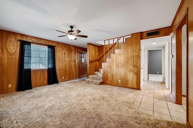 unfurnished living room featuring light colored carpet, a textured ceiling, ceiling fan, and wood walls